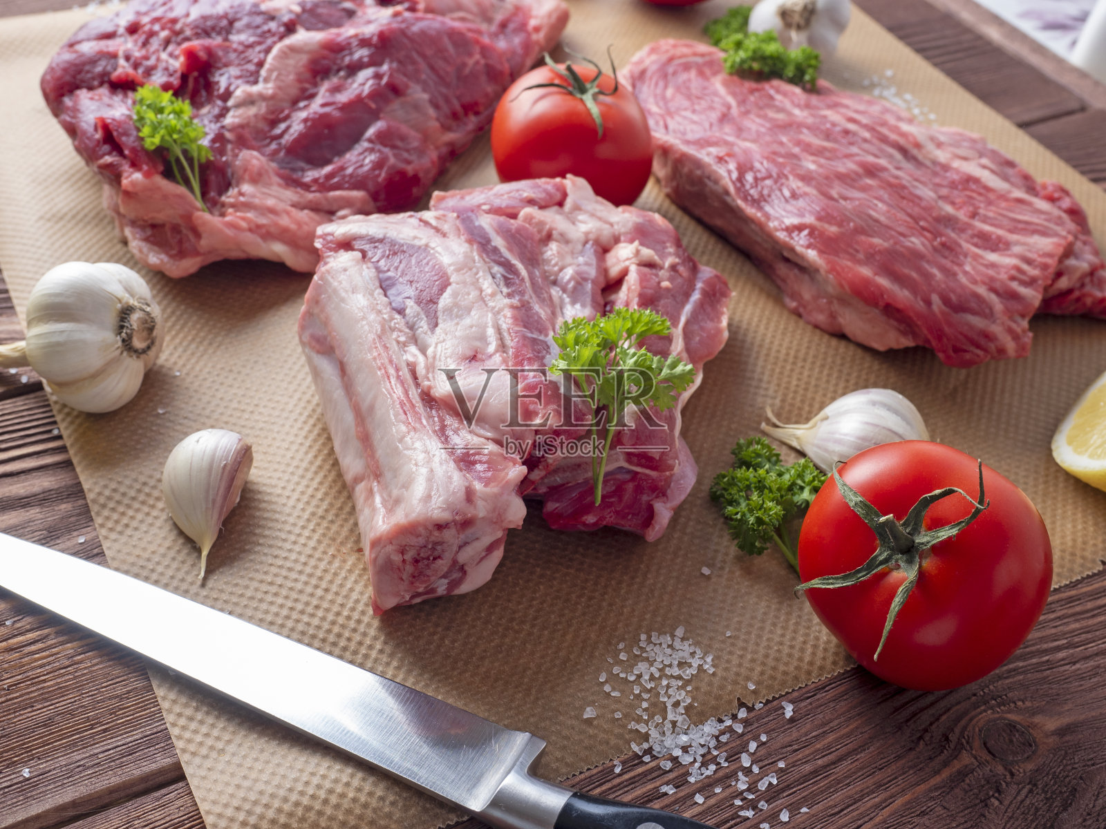 几块新鲜的生肉摊在羊皮纸上。除了大蒜，香草，西红柿和刀。侧视图。照片摄影图片