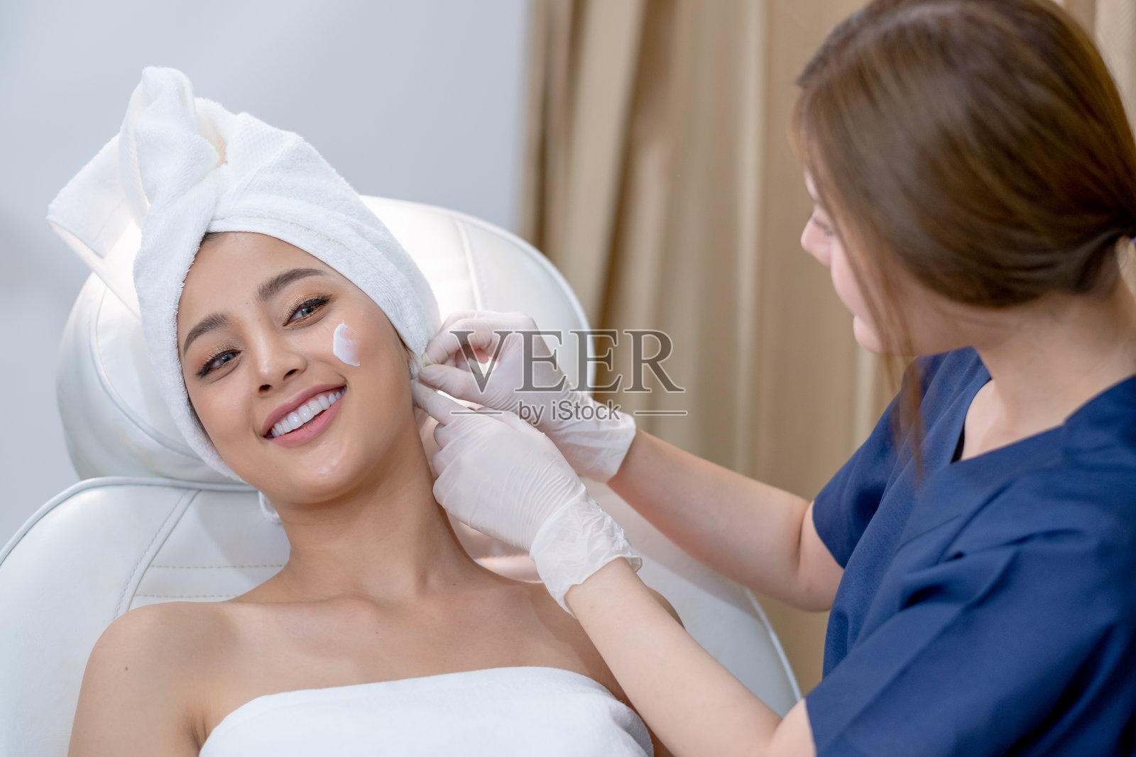 美容诊所的工作人员帮助调整和设置毛巾，以覆盖客户妇女的头发，她的客户看起来很高兴照片摄影图片