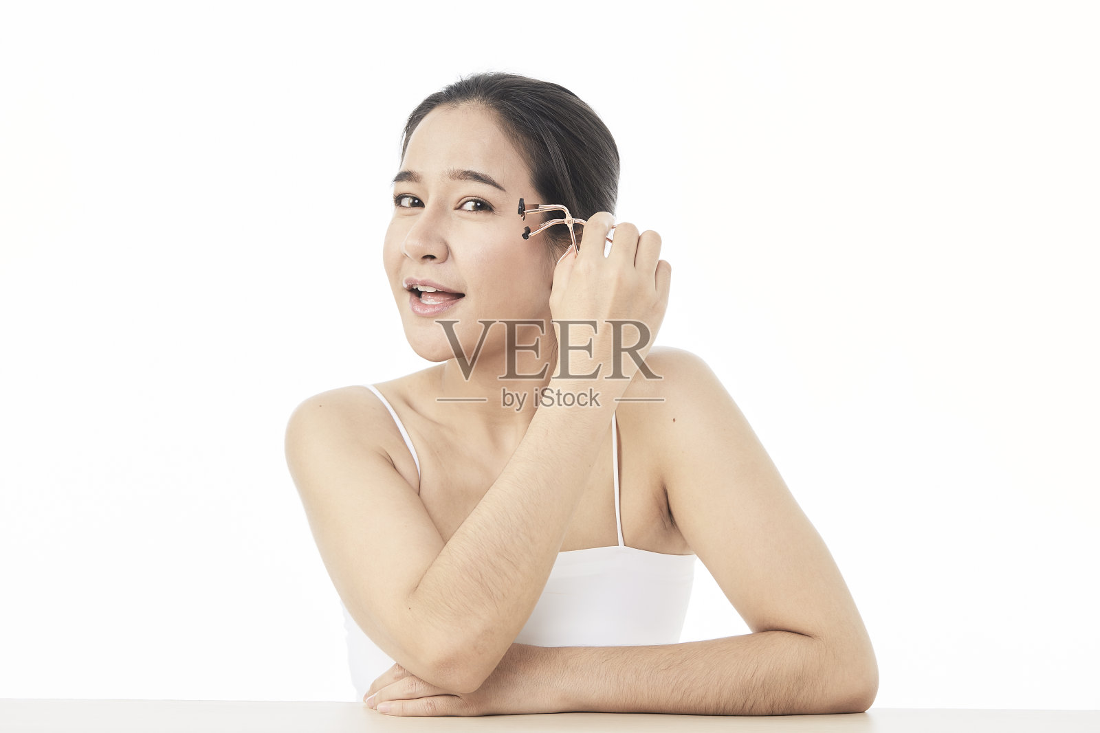 特写一个美丽的亚洲女人使用睫毛夹在白色的背景。照片摄影图片