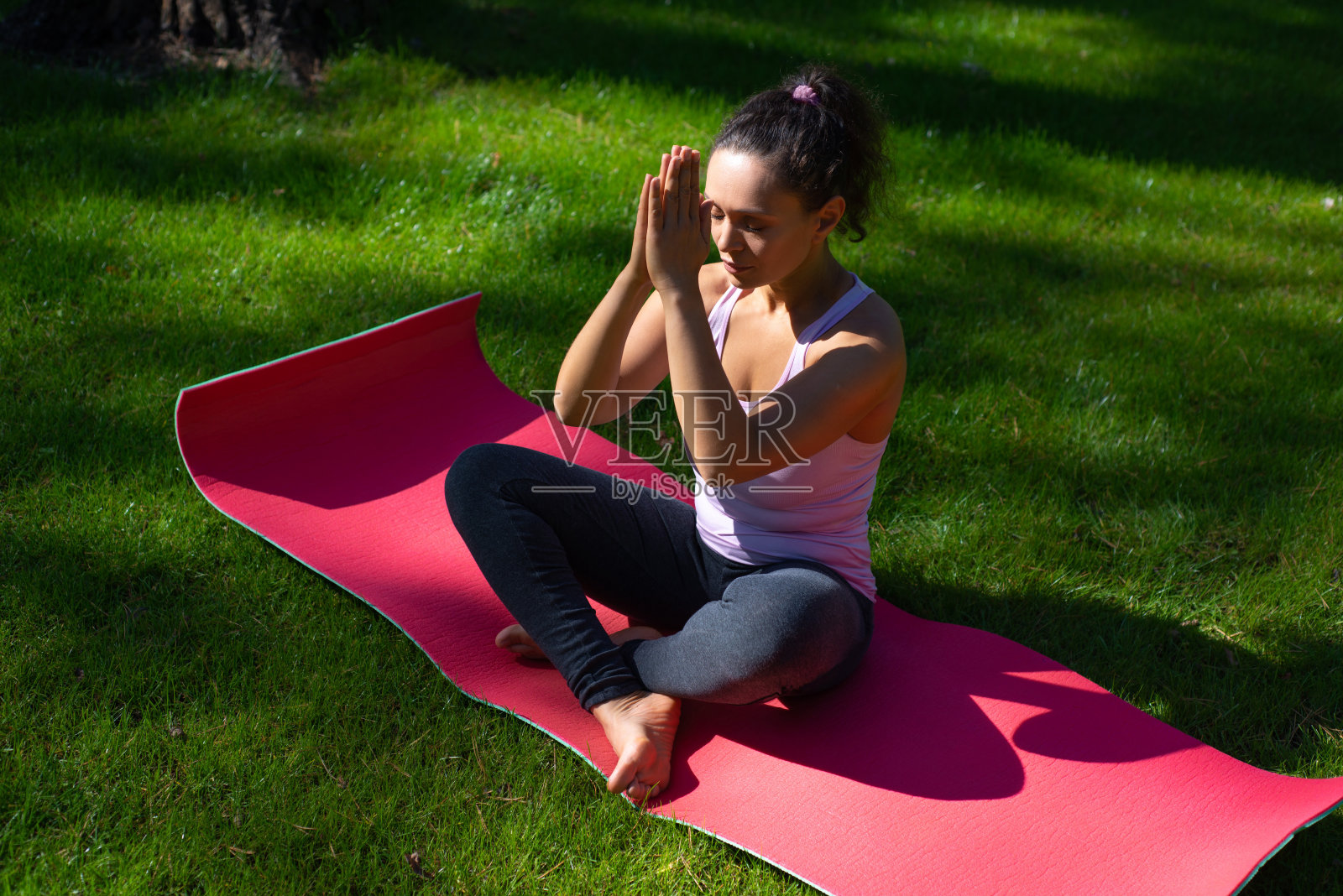 在一个温暖的日子里，一名年轻女子坐在瑜伽垫上，闭着眼睛做瑜伽照片摄影图片