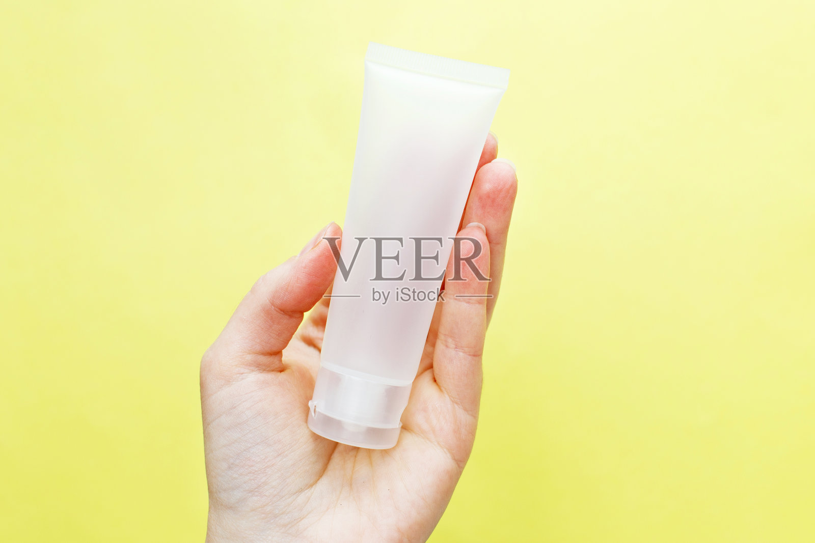 女性手拿霜筒化妆品上的黄色背景照片摄影图片