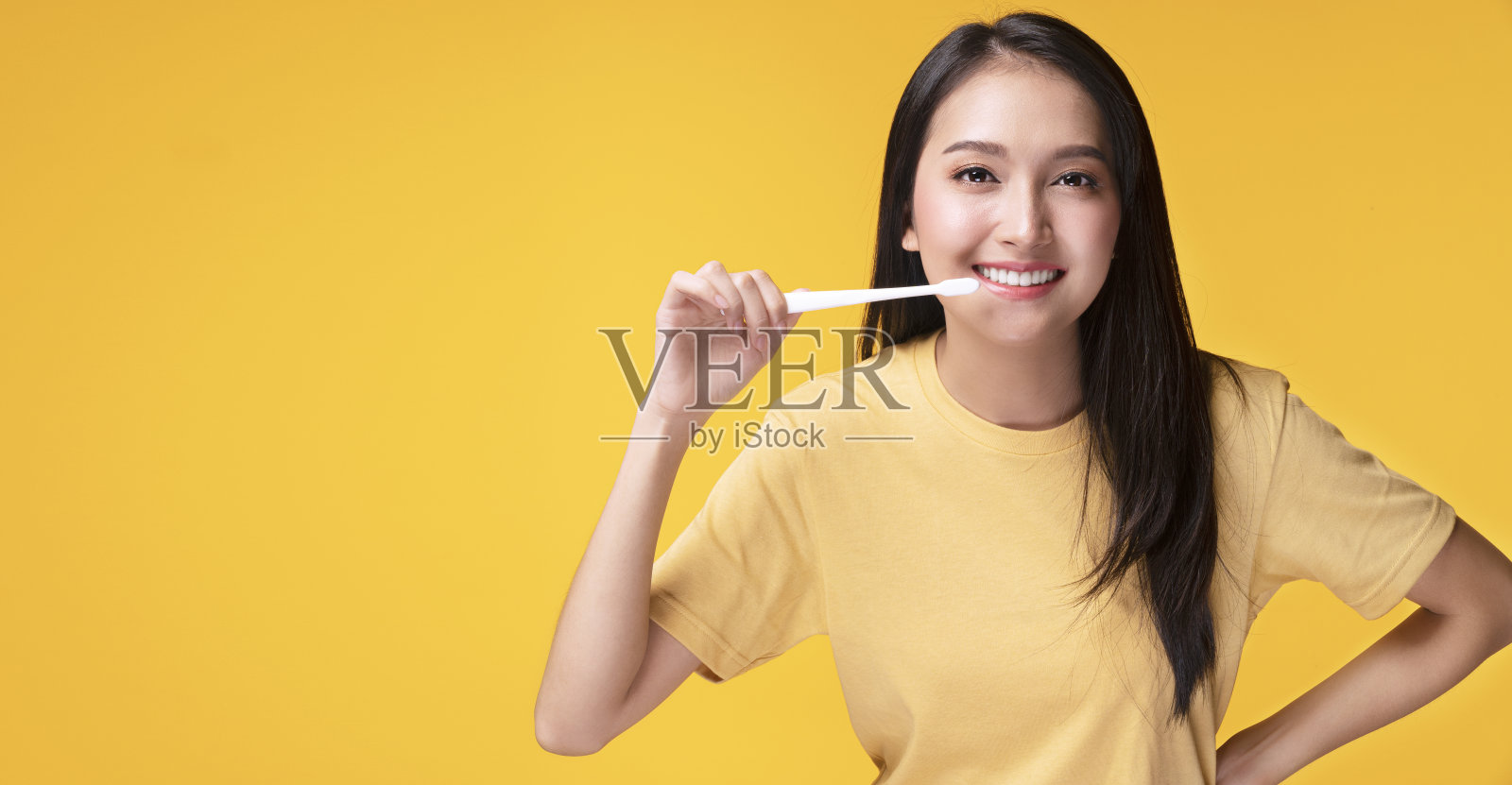 微笑的年轻女子拿着白色的牙刷在她的手，而看着相机在孤立的黄色背景与复制空间。良好的口腔和牙齿保健理念。照片摄影图片