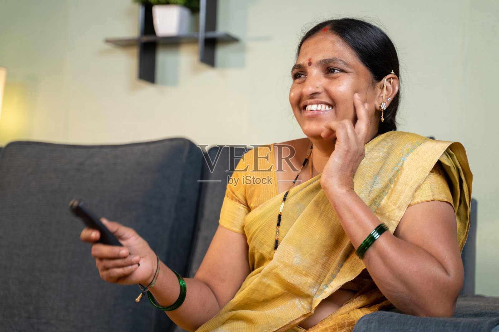 穿着纱丽的印度女人在闲暇时间坐在沙发上看电视照片摄影图片