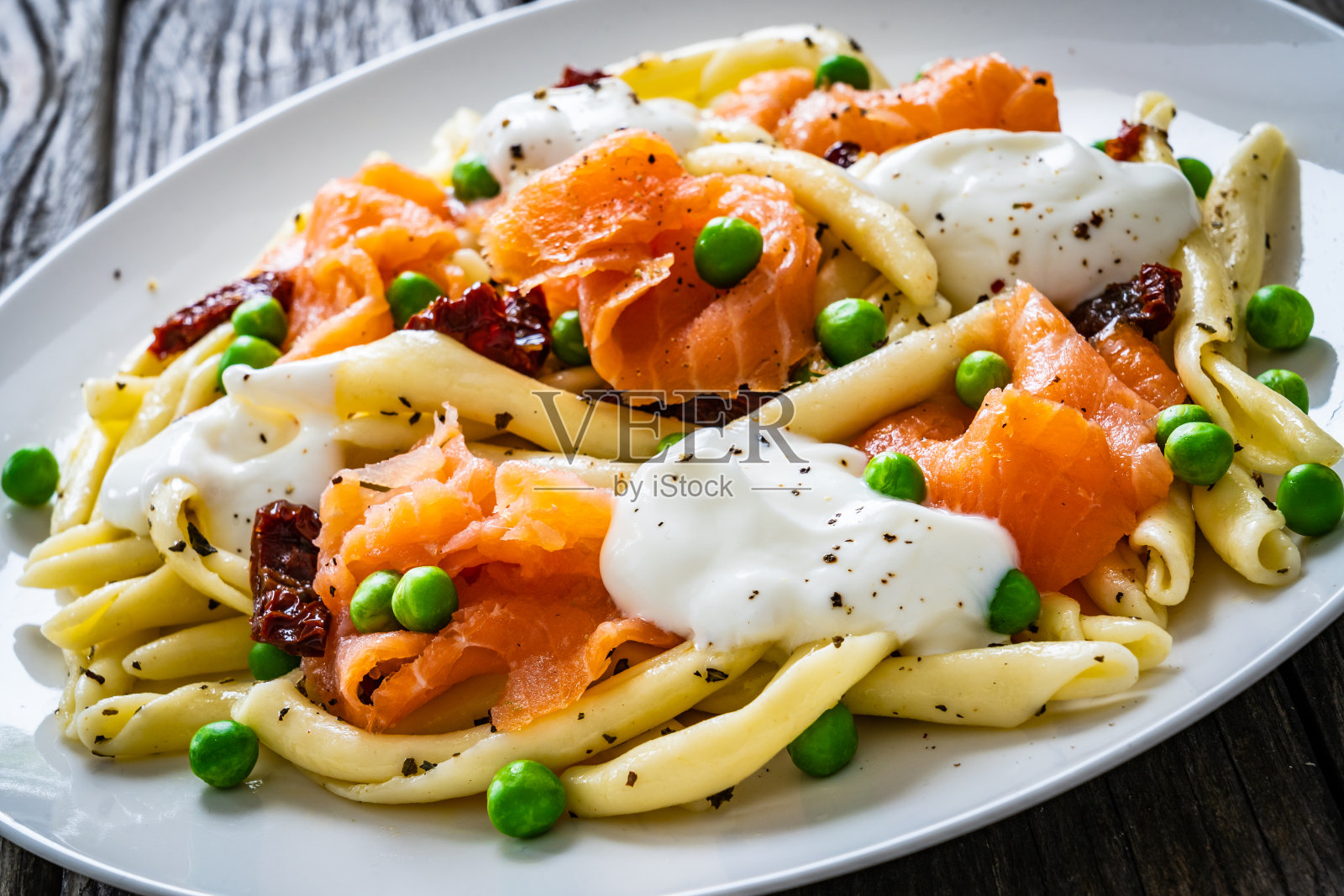 雪貂通心粉配鲑鱼块，豌豆和晒干的番茄放在木桌上照片摄影图片