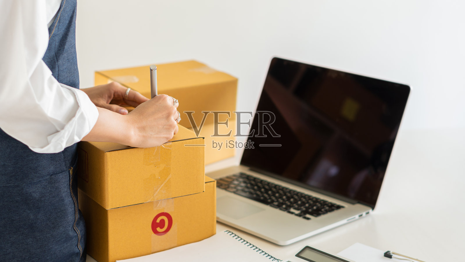 年轻的女性小企业主在纸箱上写地址，在工作中，中小企业企业家也工作在家里的盒子，是的，笔记本电脑销售网上电子商务拳击的想法照片摄影图片