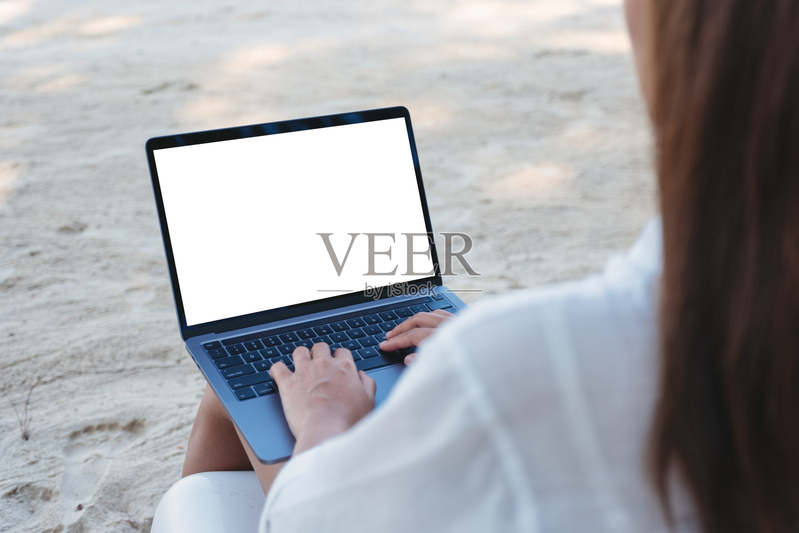 坐在海滩上的一位女士正在用笔记本电脑打字，桌面是空白的照片摄影图片