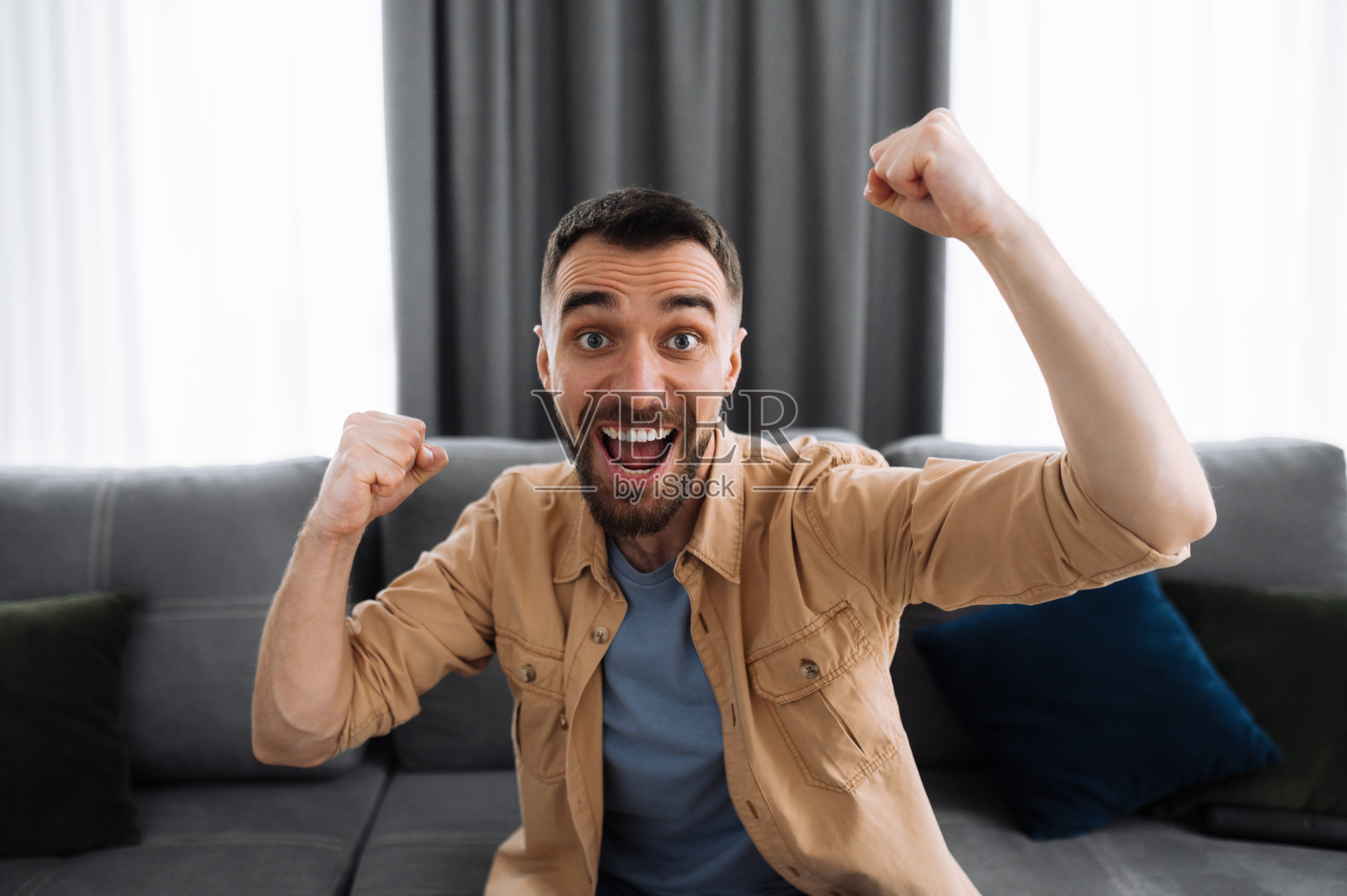 情绪激动的男人在看电视，支持和为喜欢的球队欢呼。兴奋愉快的男性坐在家里的沙发上，庆祝比赛的结果，或得到一个好消息或交易照片摄影图片