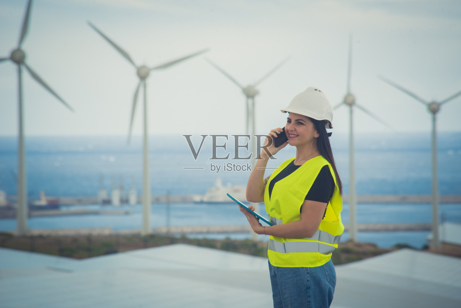 成年女性工程师在一个可再生能源综合设施中管理太阳能电池板和风车照片摄影图片
