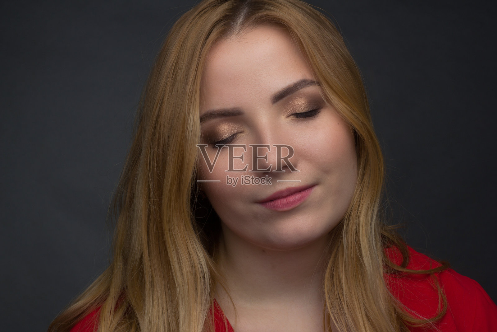 一个肥胖的金发女孩，在黑暗的工作室背景上穿着红色的外套照片摄影图片