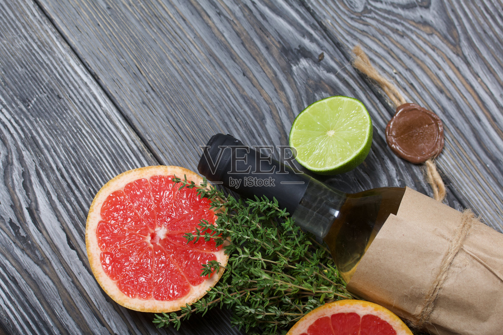 酒精瓶。包裹在纸上。旁边放着百里香，半块酸橙和葡萄柚。松木板。照片摄影图片