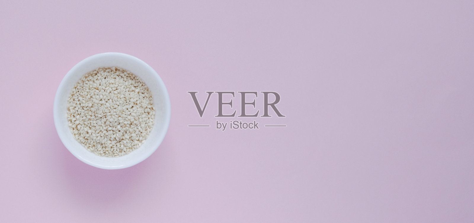 白色的芝麻，在一个小杯子里，在粉红色的背景上照片摄影图片