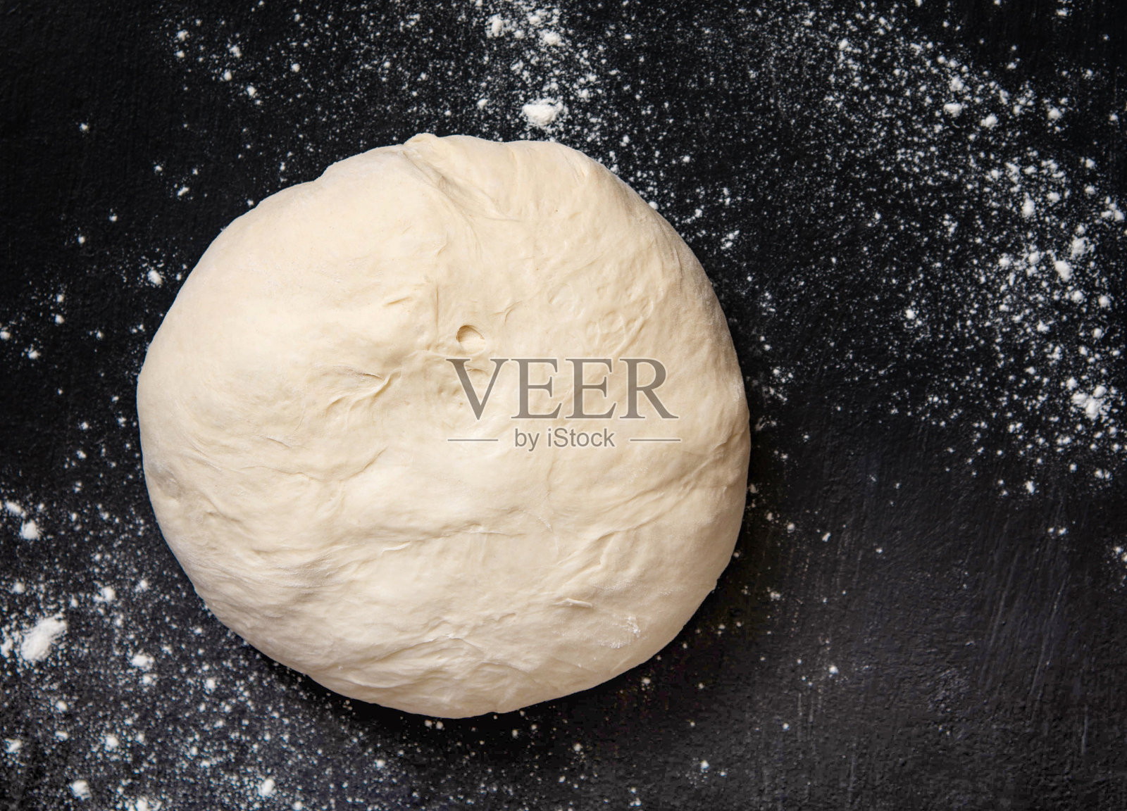 发酵面团放在撒有面粉的黑面上，用于制作面包或披萨照片摄影图片