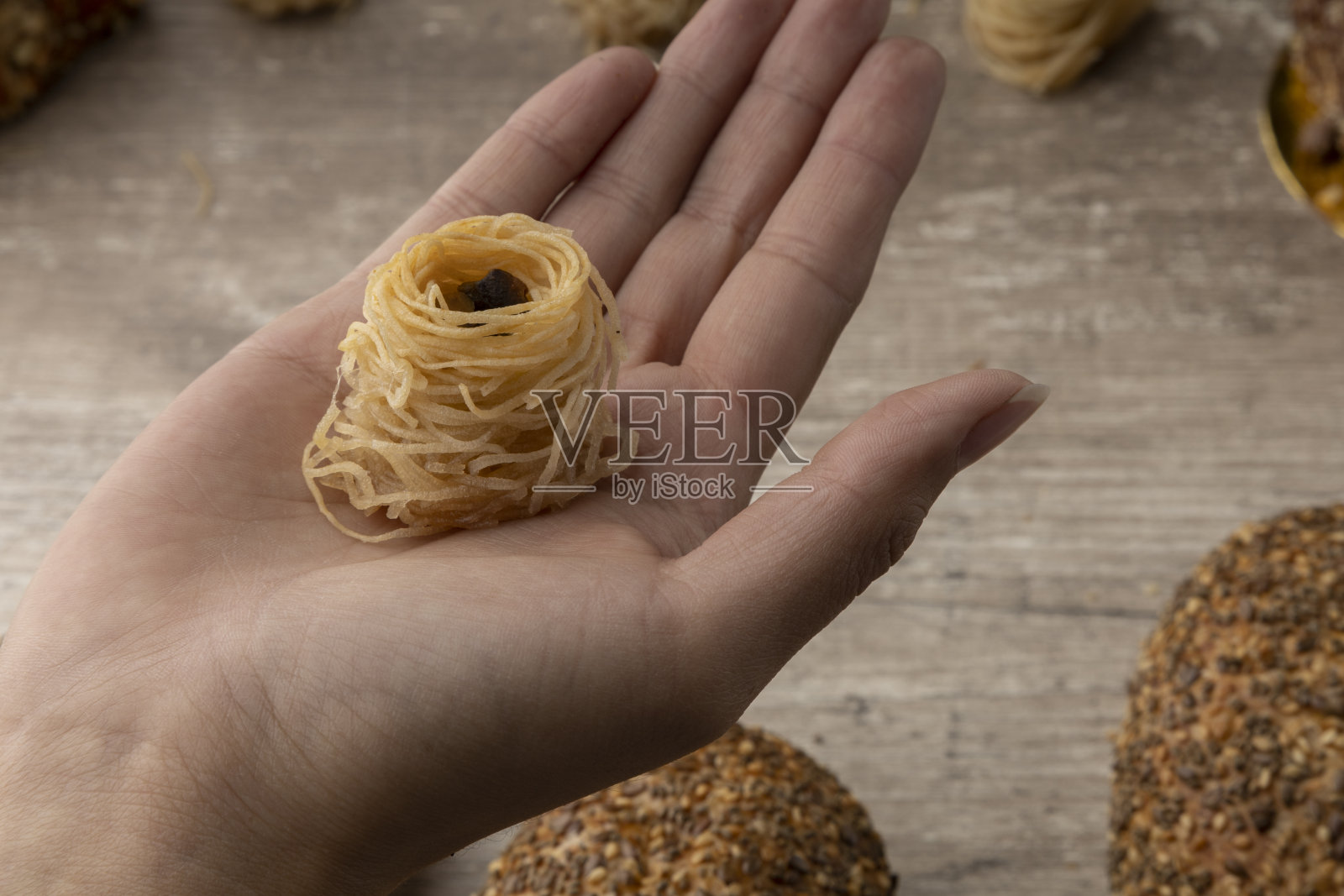 手掌握着一个巢状的阿拉伯甜点，木制的背景和面包，工作室照片摄影图片