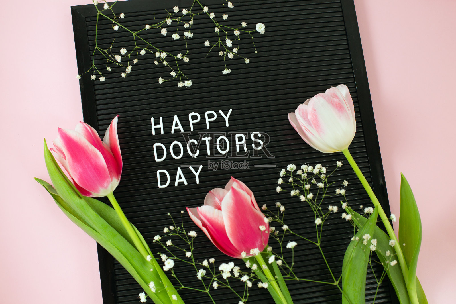 黑色的信纸和白色的塑料字母，上面写着“医生的一天快乐”和粉红色背景上的一束粉红色郁金香。照片摄影图片