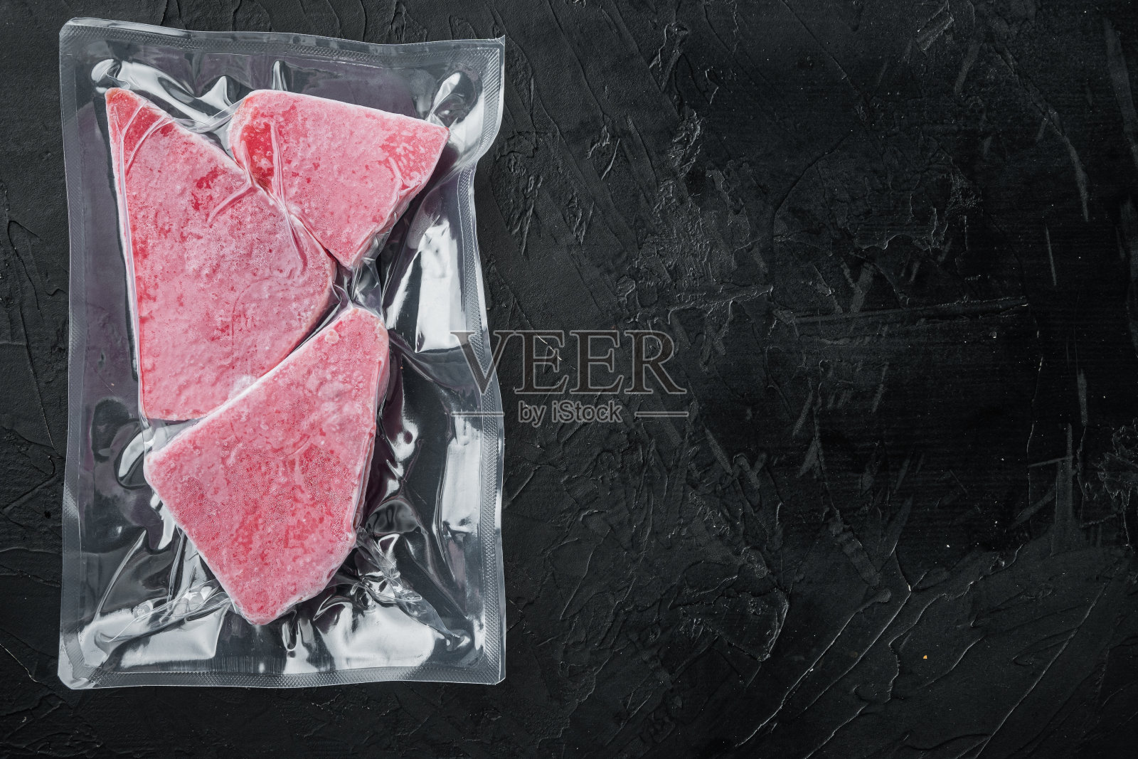 冷冻金枪鱼排在真空塑料包装，在黑色的石头背景，俯视图平lay，与copyspace和文本空间照片摄影图片