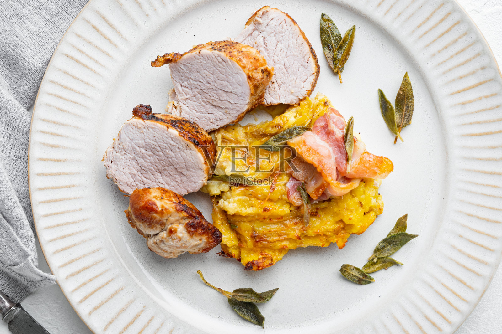 烤猪里脊配土豆泥，鼠尾草和熏火腿，放在盘子里，白石背景上，俯视图平铺照片摄影图片