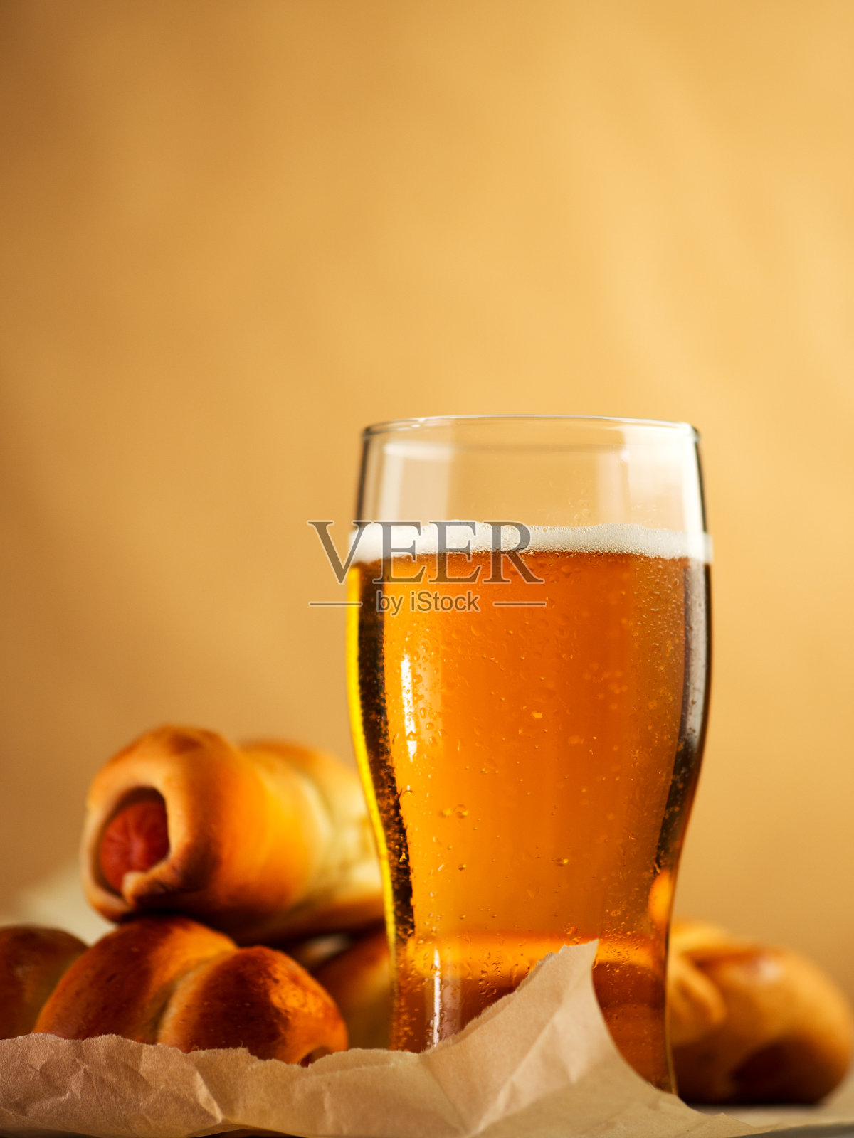 桌上放着一杯淡啤酒，香肠放在生面团里作开胃菜。黄色背景。照片摄影图片