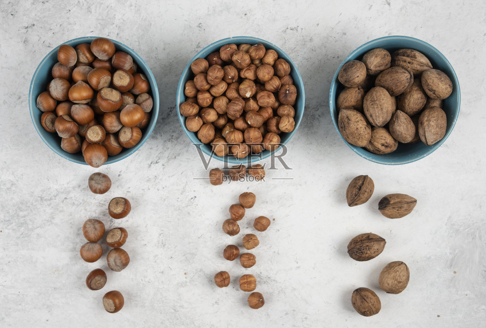 大理石背景上放着几碗蓝色的核桃、榛子和果仁照片摄影图片