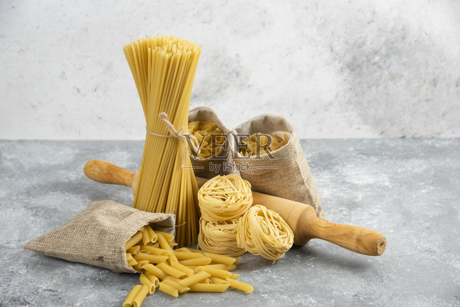 各种各样的意大利面在乡村篮子与木滚动粉红色大理石背景照片摄影图片