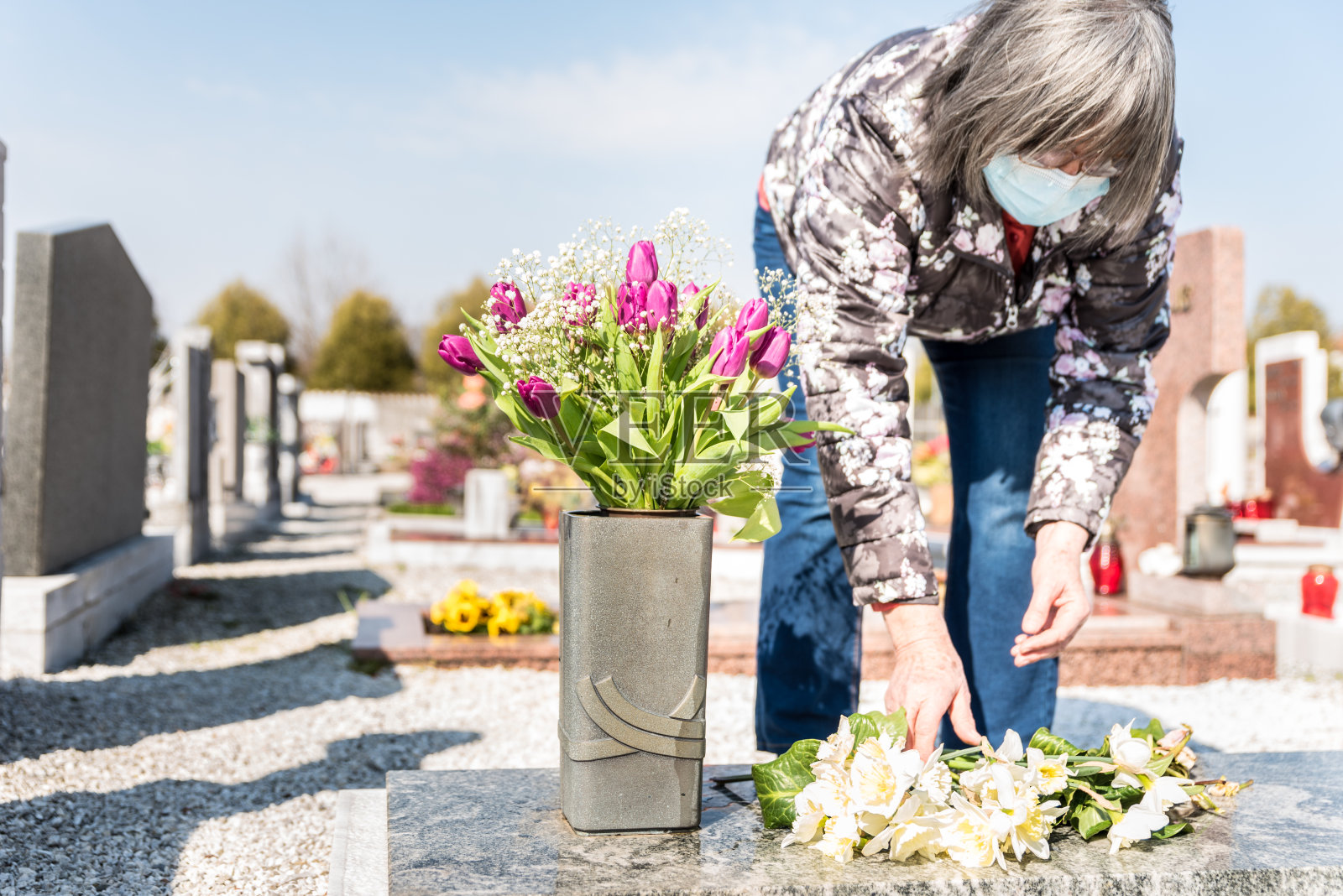 2019冠状病毒病大流行期间，老妇人带着鲜花来到墓地照片摄影图片