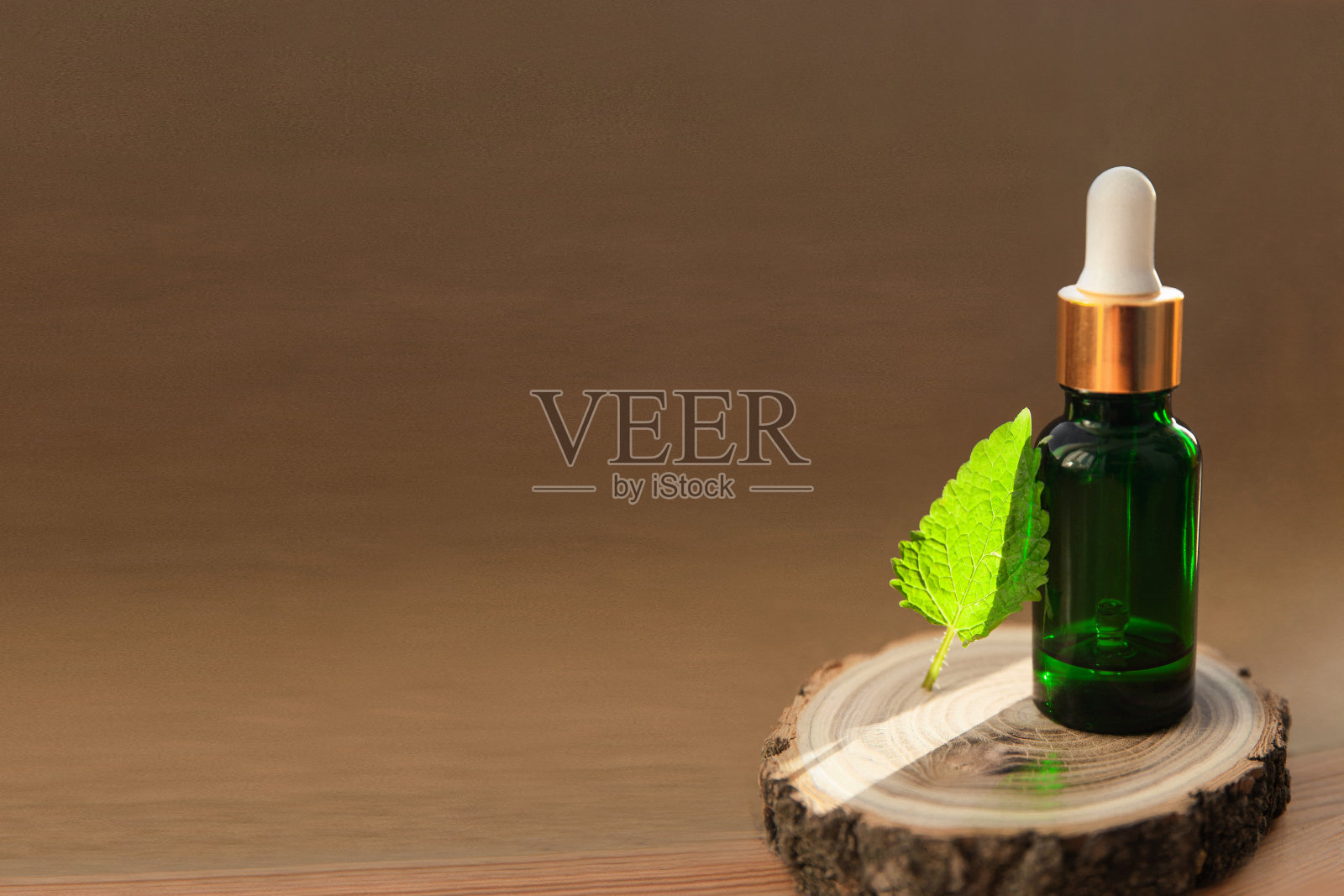 在阳光下的木片上放着一瓶绿色的玻璃薄荷油和一片新鲜的叶子照片摄影图片