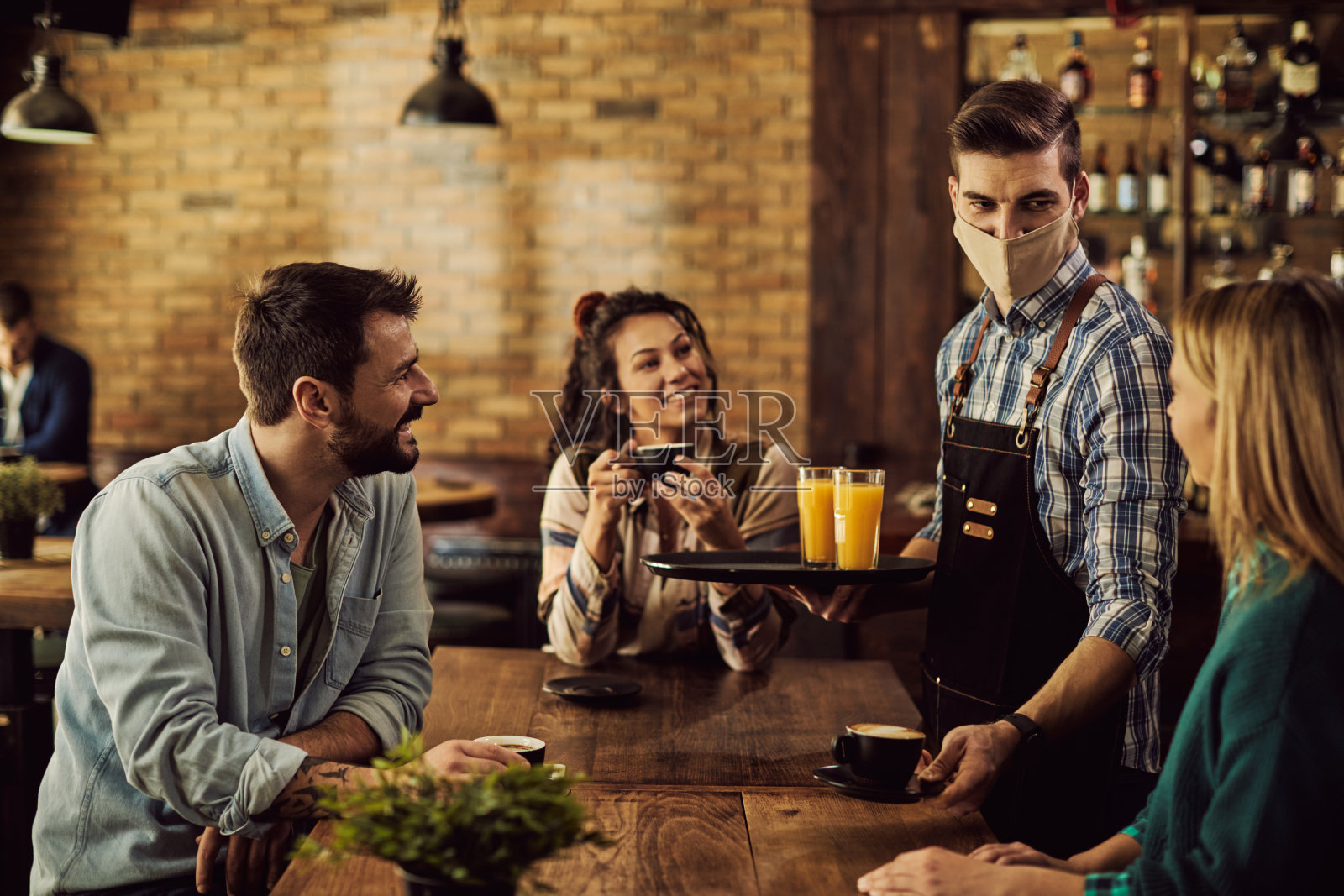 在酒吧里，带着保护面罩的服务员为顾客端咖啡。照片摄影图片