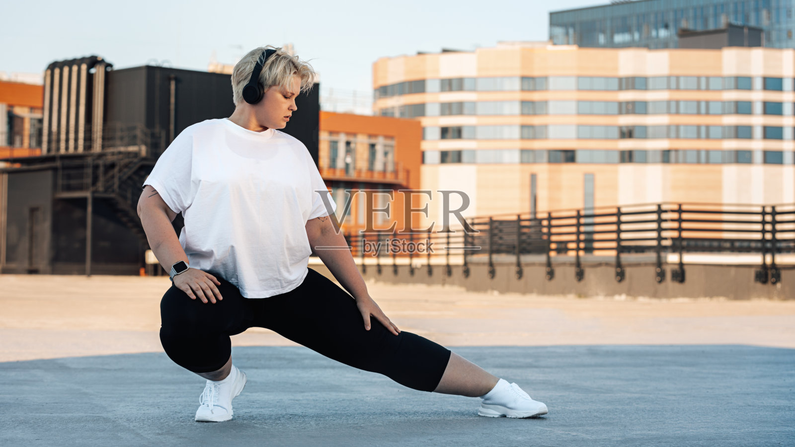 胖女人伸展她的腿。年轻的曲线女性在屋顶上锻炼。照片摄影图片