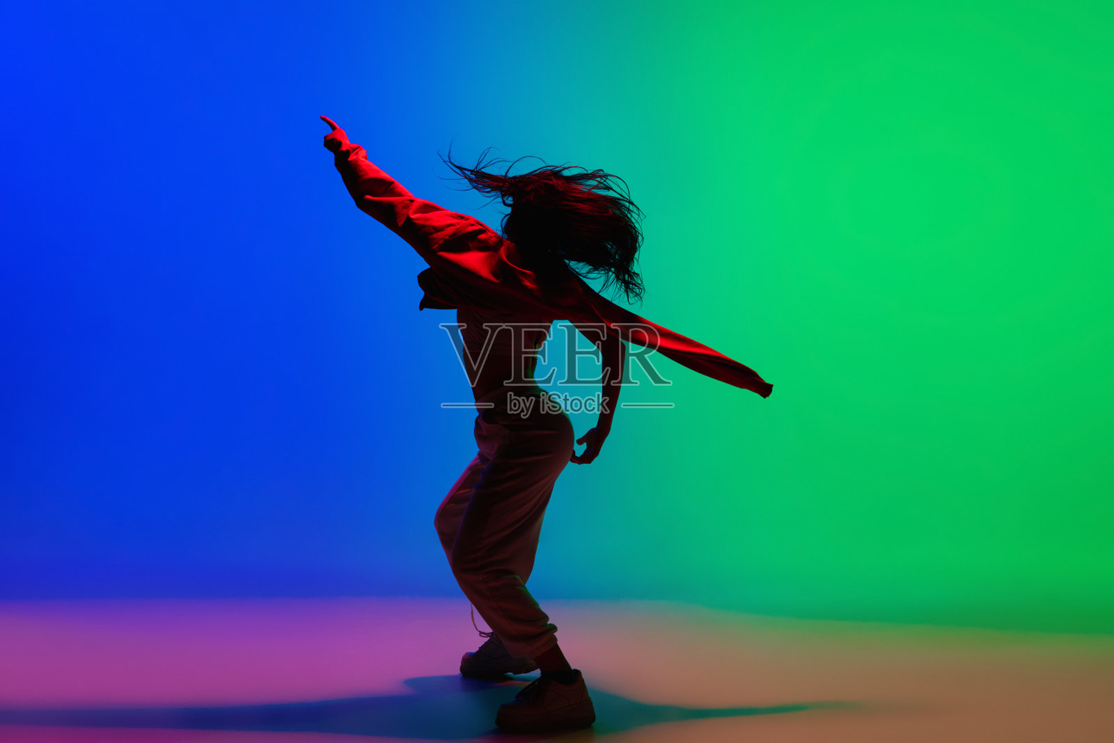 在霓虹灯下的舞厅里，时尚的运动女孩穿着时尚的衣服在五颜六色的背景下跳嘻哈舞。青年文化、运动、风格、时尚、行动。照片摄影图片