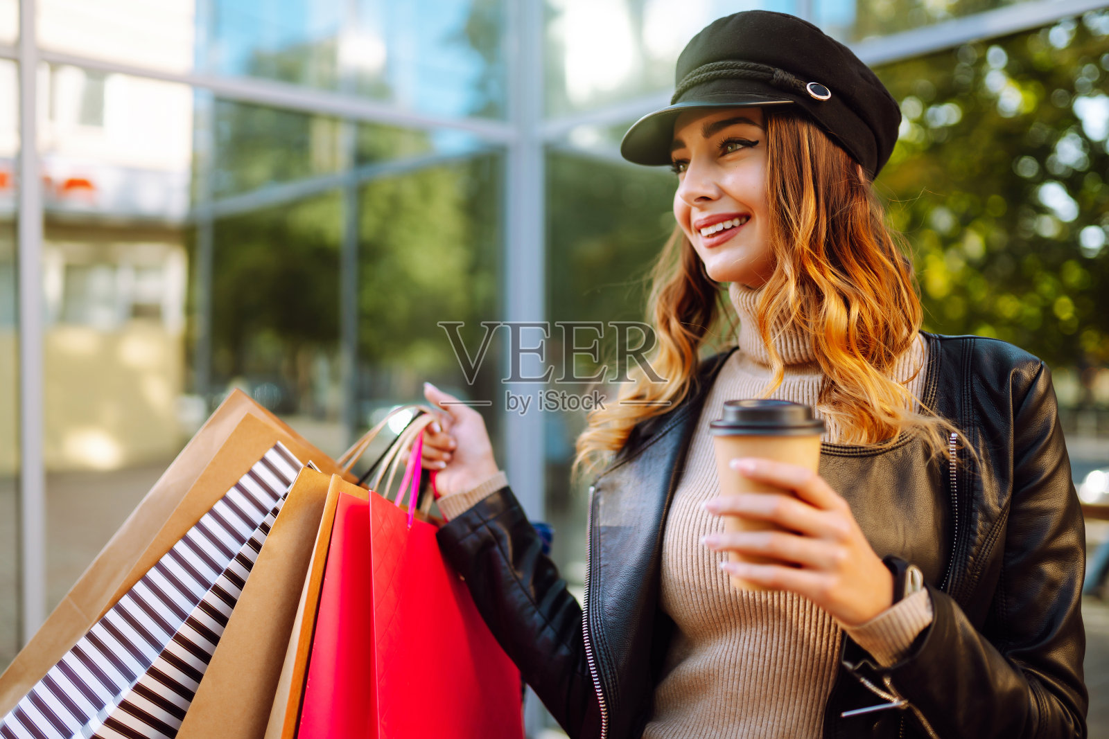 年轻女子购物后在城市街道上喝咖啡。拎着购物袋的时髦女人。照片摄影图片