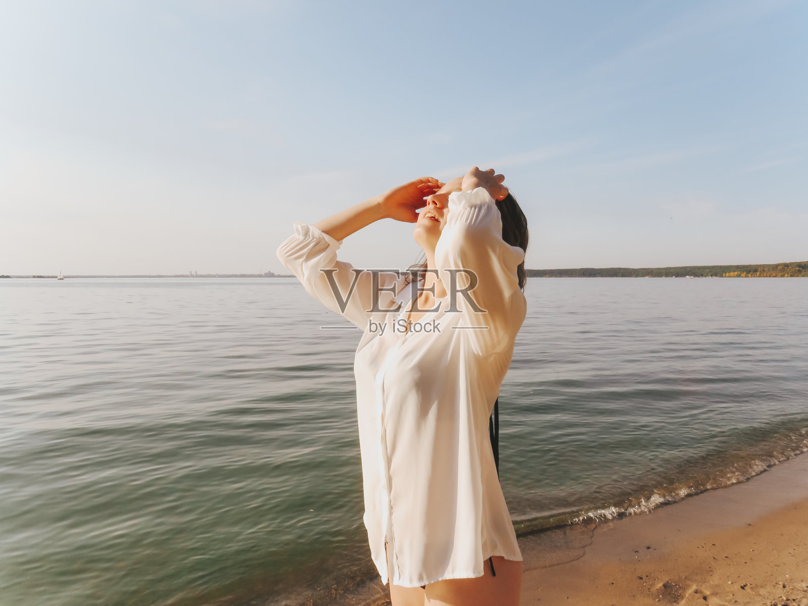 快乐的年轻女子穿着白色的衬衫和比基尼在日落的海边，情绪幸福，快乐，自由照片摄影图片