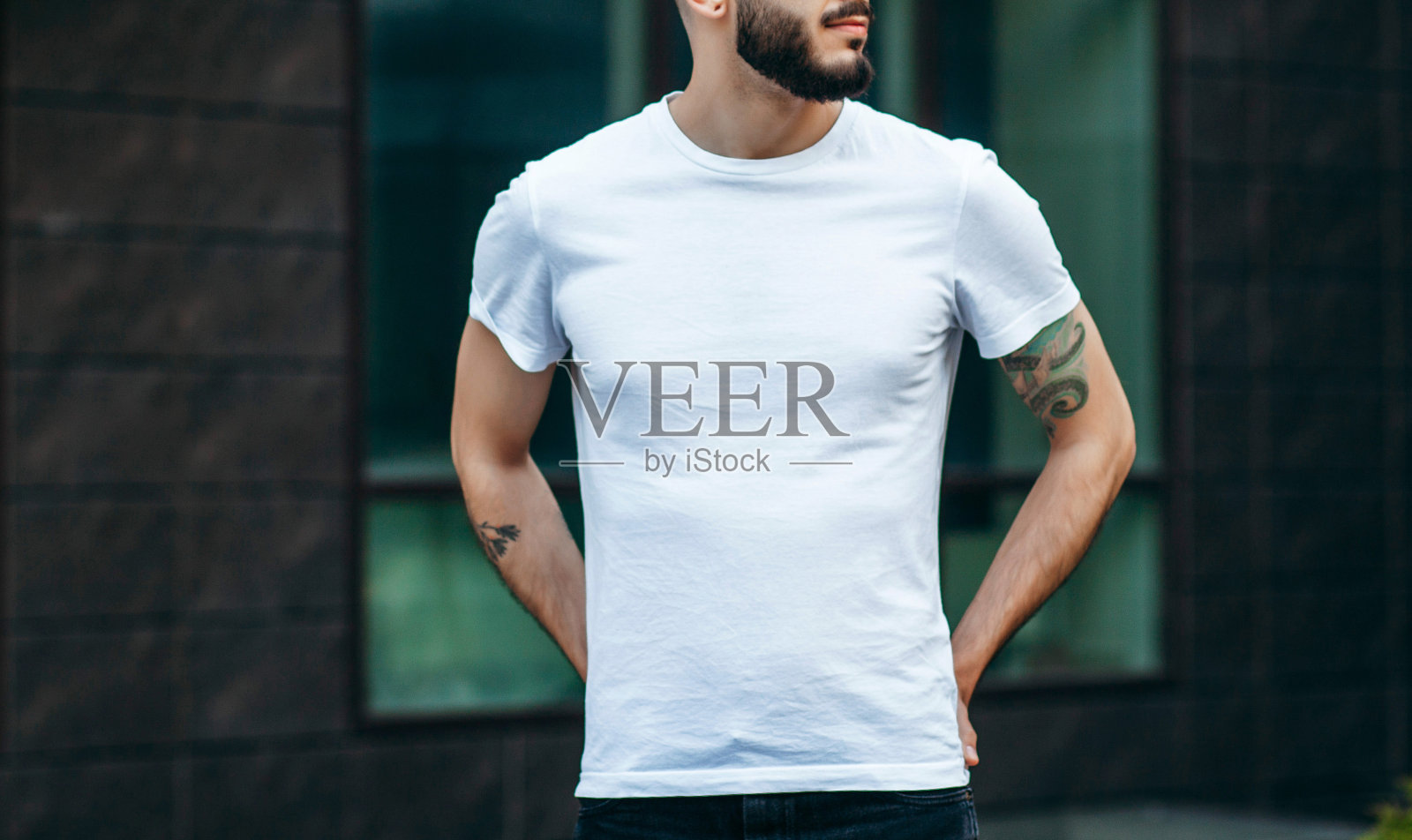 一个留着胡子，穿着白色t恤，戴着眼镜的年轻时髦的男人。街头的照片照片摄影图片