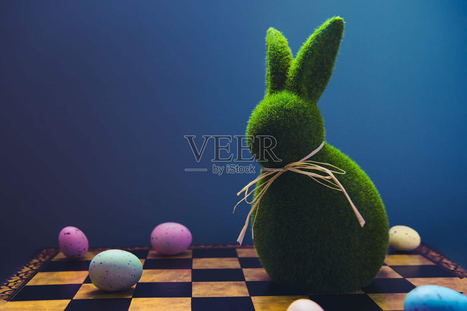 创意和流行的复活节概念。复活节棋类游戏与彩蛋和复活节兔子绿色兔子在深蓝色的背景。选择性聚焦，复制空间。照片摄影图片