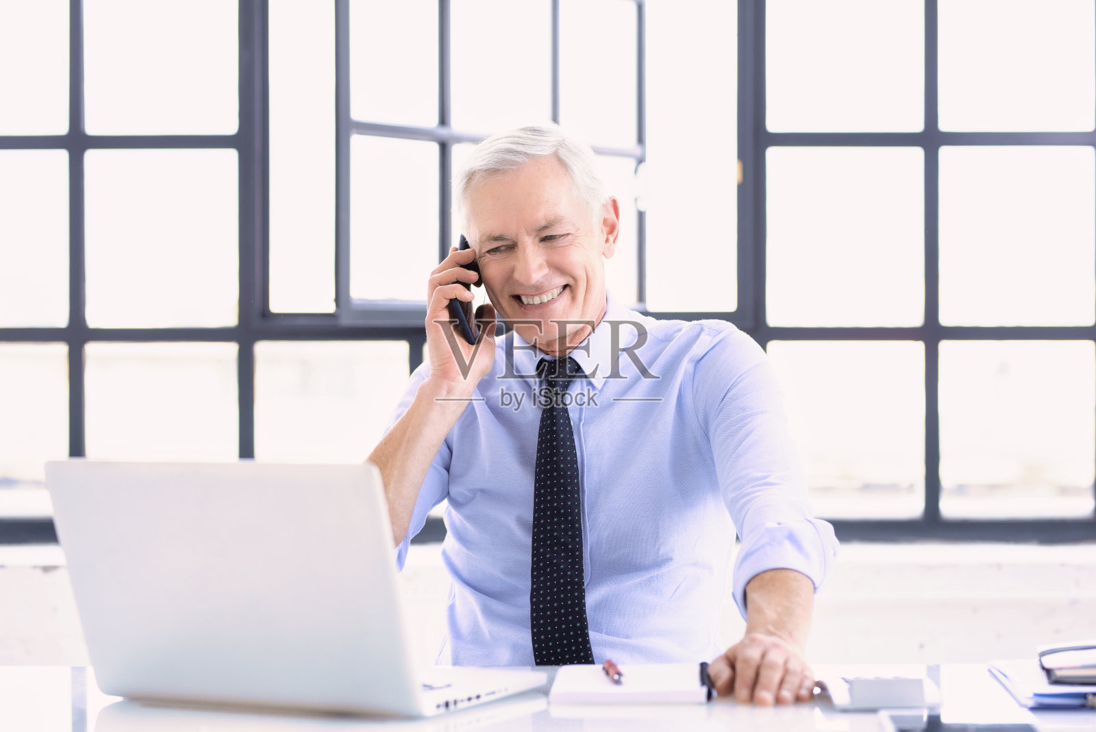 这是一位高级商人在办公室工作时使用笔记本电脑打电话的照片照片摄影图片