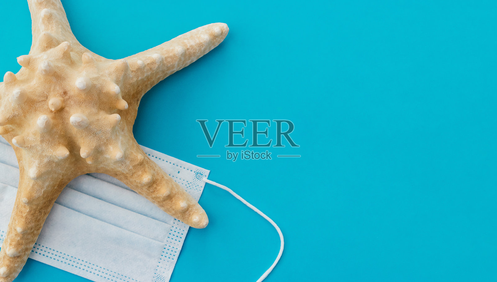 蓝色背景上的海星和防护面具。因新冠肺炎大流行取消暑假和旅游的概念。夏天的概念。选择性聚焦，俯视图，复制空间照片摄影图片