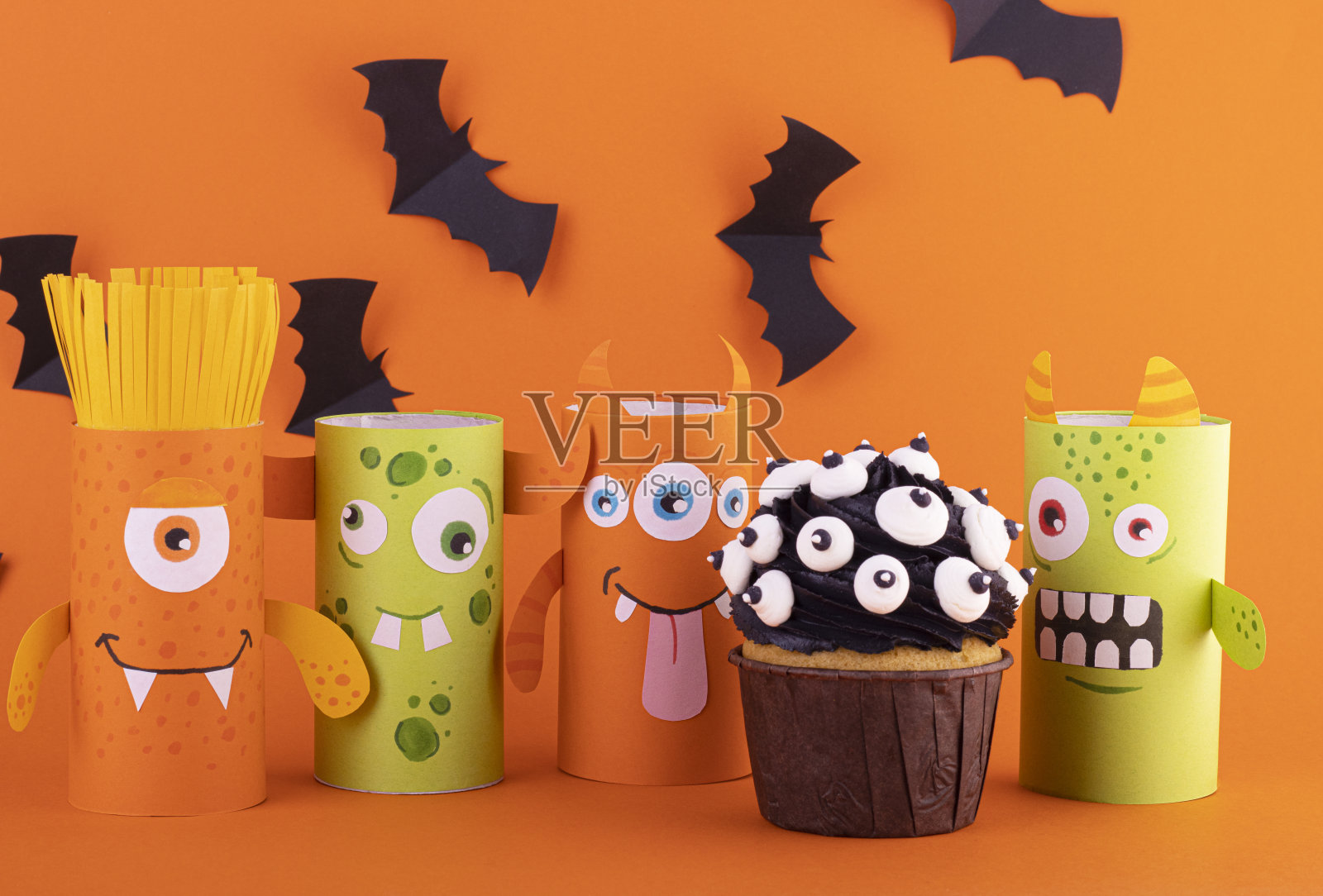 纸鬼，一个可怕的手工制作的怪物，在橙色的背景上有一个黑色的纸杯蛋糕和黑色的蜘蛛照片摄影图片