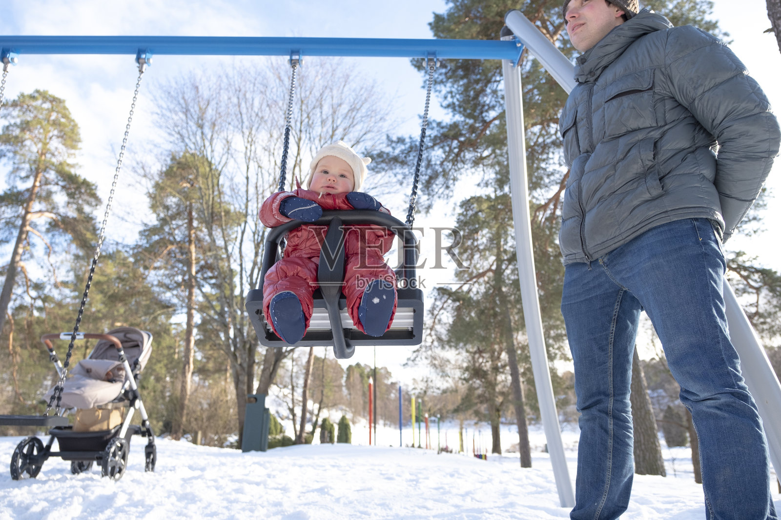 一个白人家庭在操场上。一个年轻人在儿童秋千上摇着一个婴儿。照片摄影图片