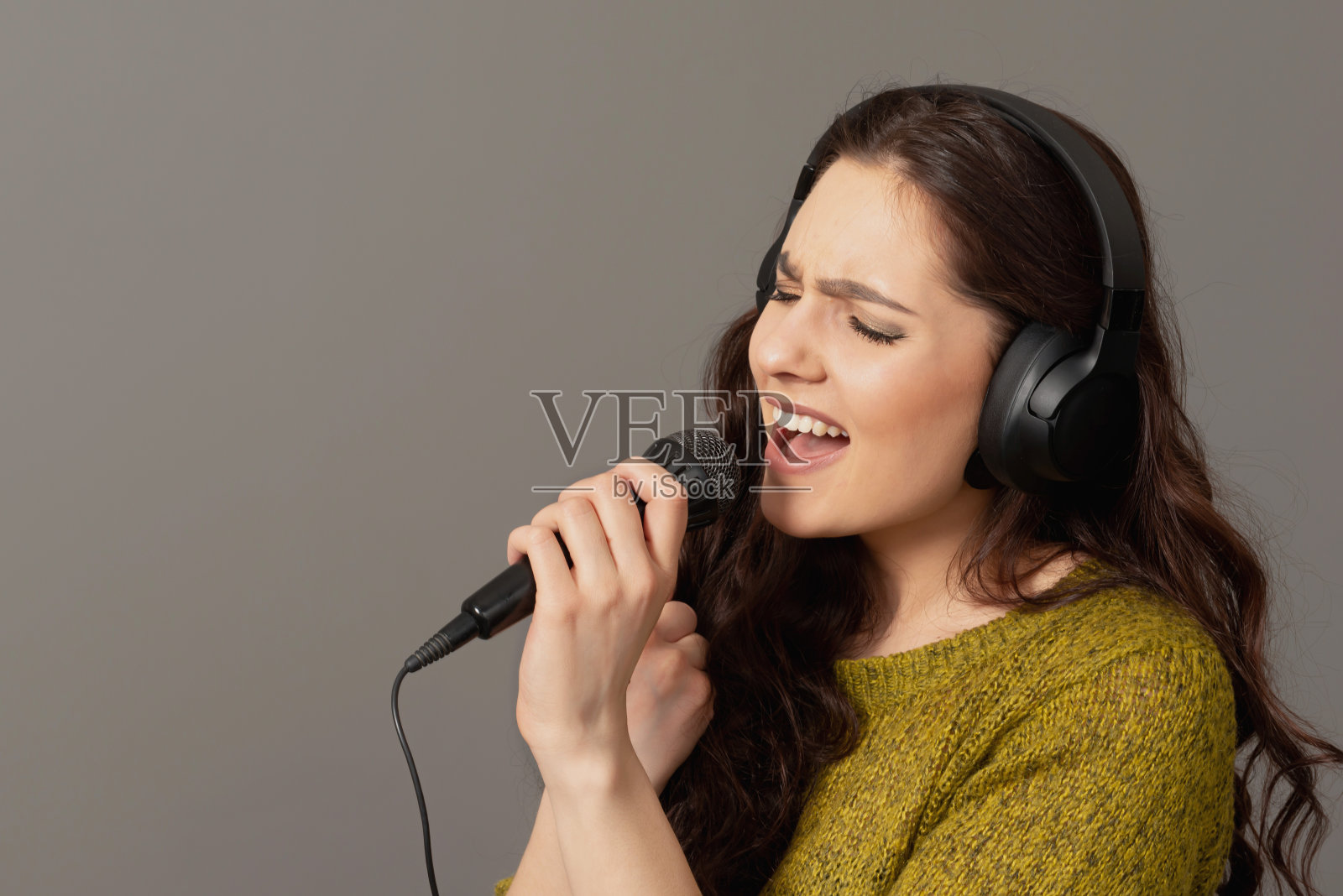 开朗的年轻女子穿着休闲装戴着耳机在麦克风里唱歌，模仿拷贝空间照片摄影图片