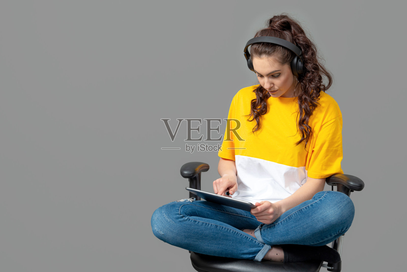 一名穿着黄色t恤的少年，一头卷发，坐在办公椅上使用平板电脑照片摄影图片