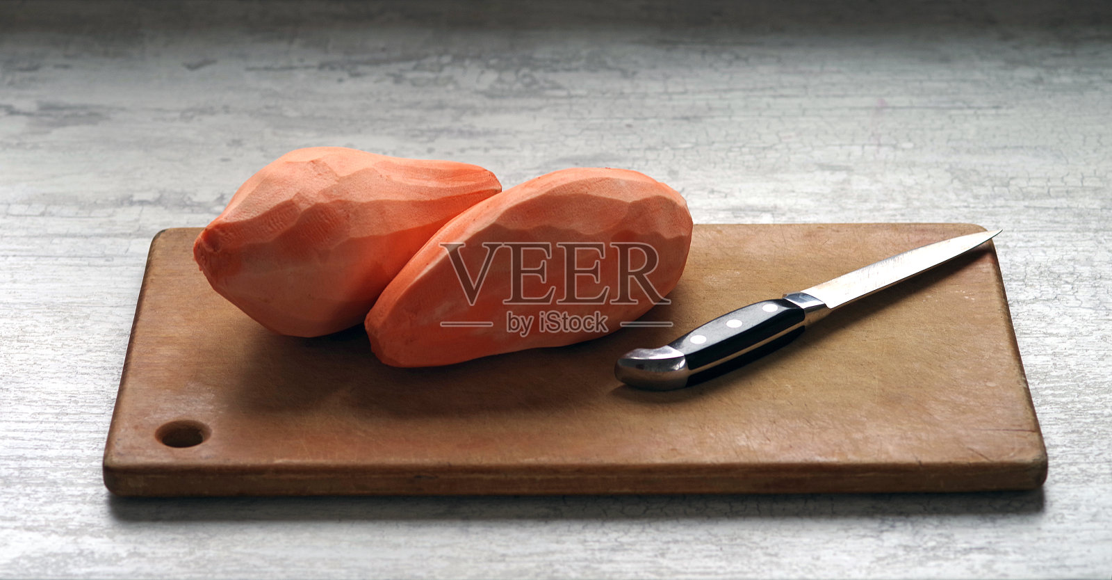 去皮的甘薯根用刀放在砧板上。照片摄影图片