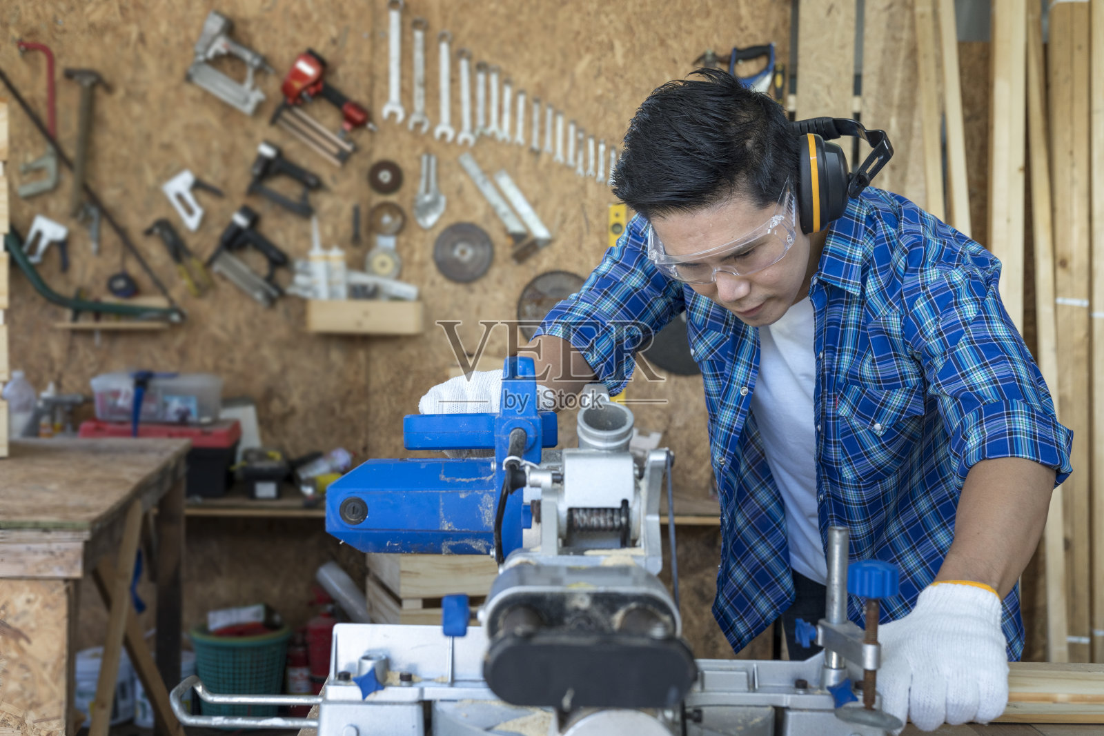 木匠用圆锯切割木头。年轻的男木匠在木工车间工作。照片摄影图片