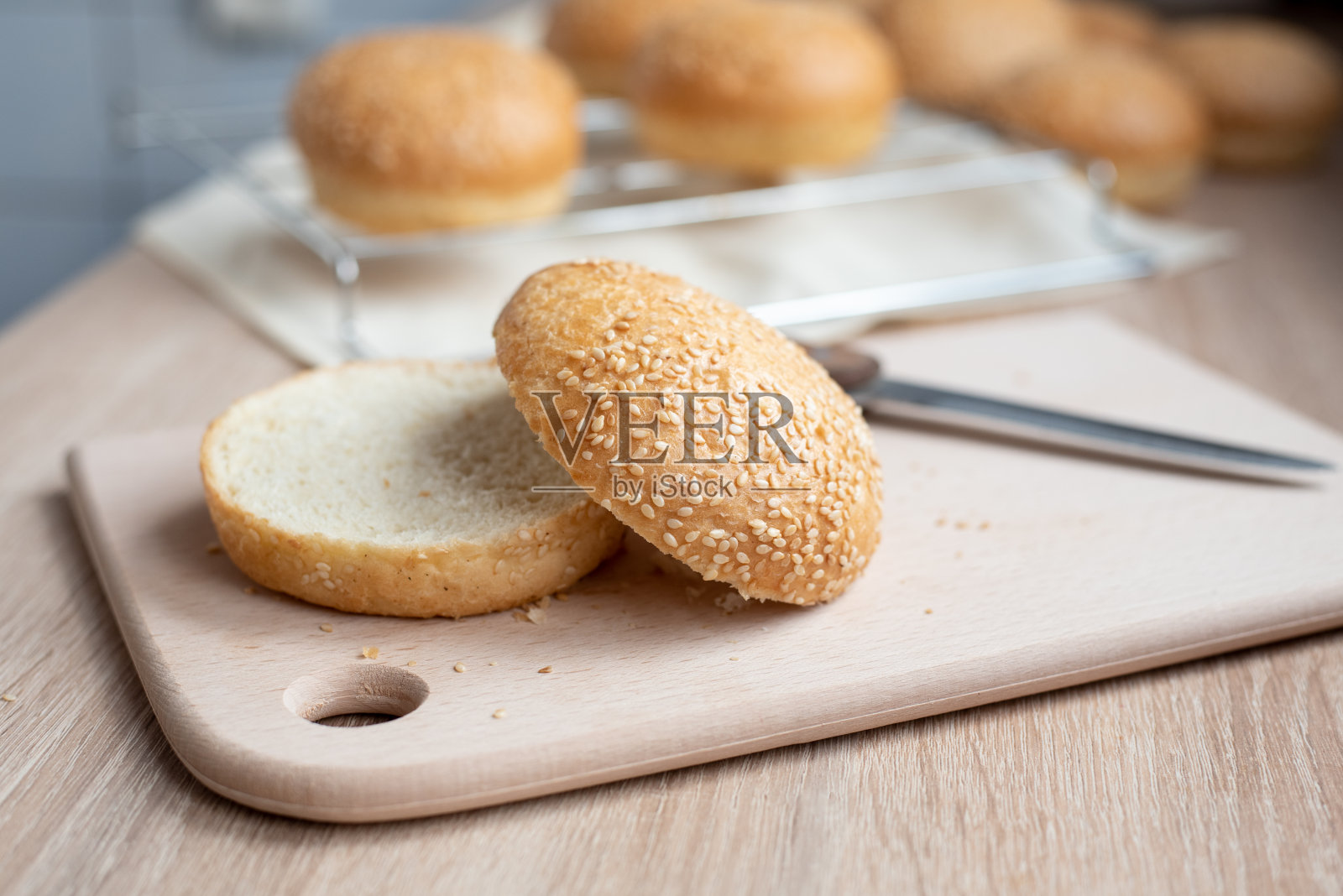 芝麻汉堡面包在厨房的木板上切成两半，在家做饭。照片摄影图片