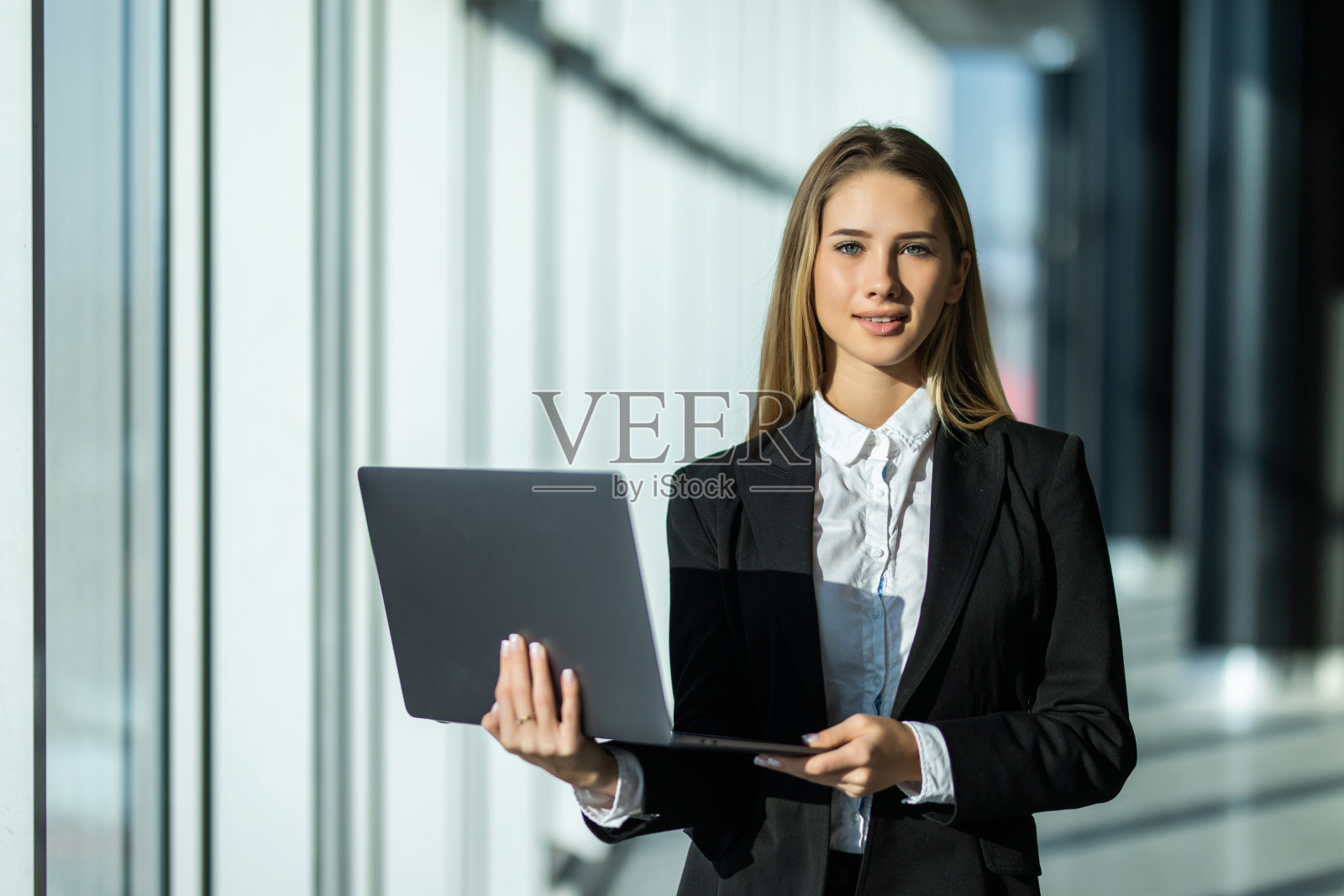 一个年轻女子的肖像，拿着笔记本电脑，站在城市全景窗口照片摄影图片