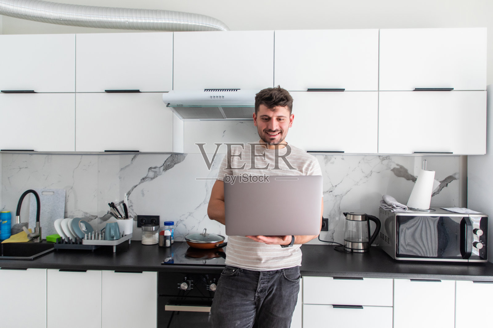 在厨房里用笔记本电脑的帅哥。在隔离禁闭中在家工作社交距离自我隔离照片摄影图片