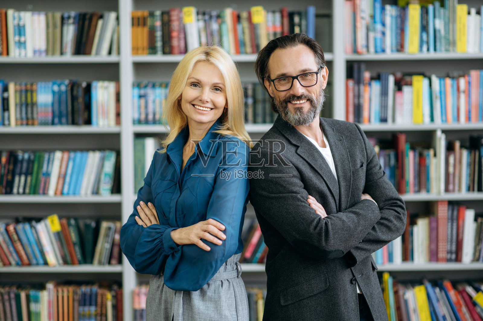 成熟成功的商业伙伴双臂交叉站在现代办公室的肖像。优雅的男女同事穿着正装直视镜头，面带微笑，团队协作理念照片摄影图片