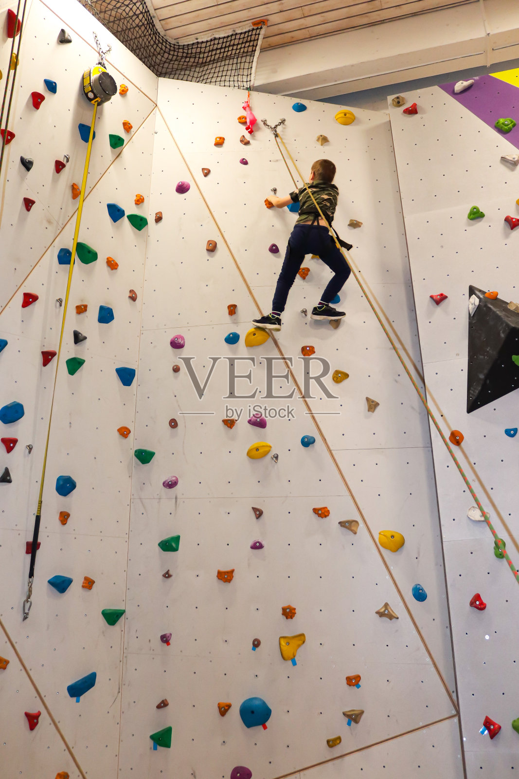小男孩在攀岩墙上用绳子攀爬照片摄影图片
