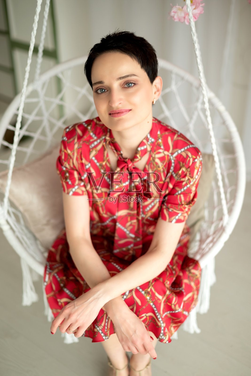 年轻迷人的黑发女子穿着红色连衣裙坐在柳条秋千上看着相机照片摄影图片