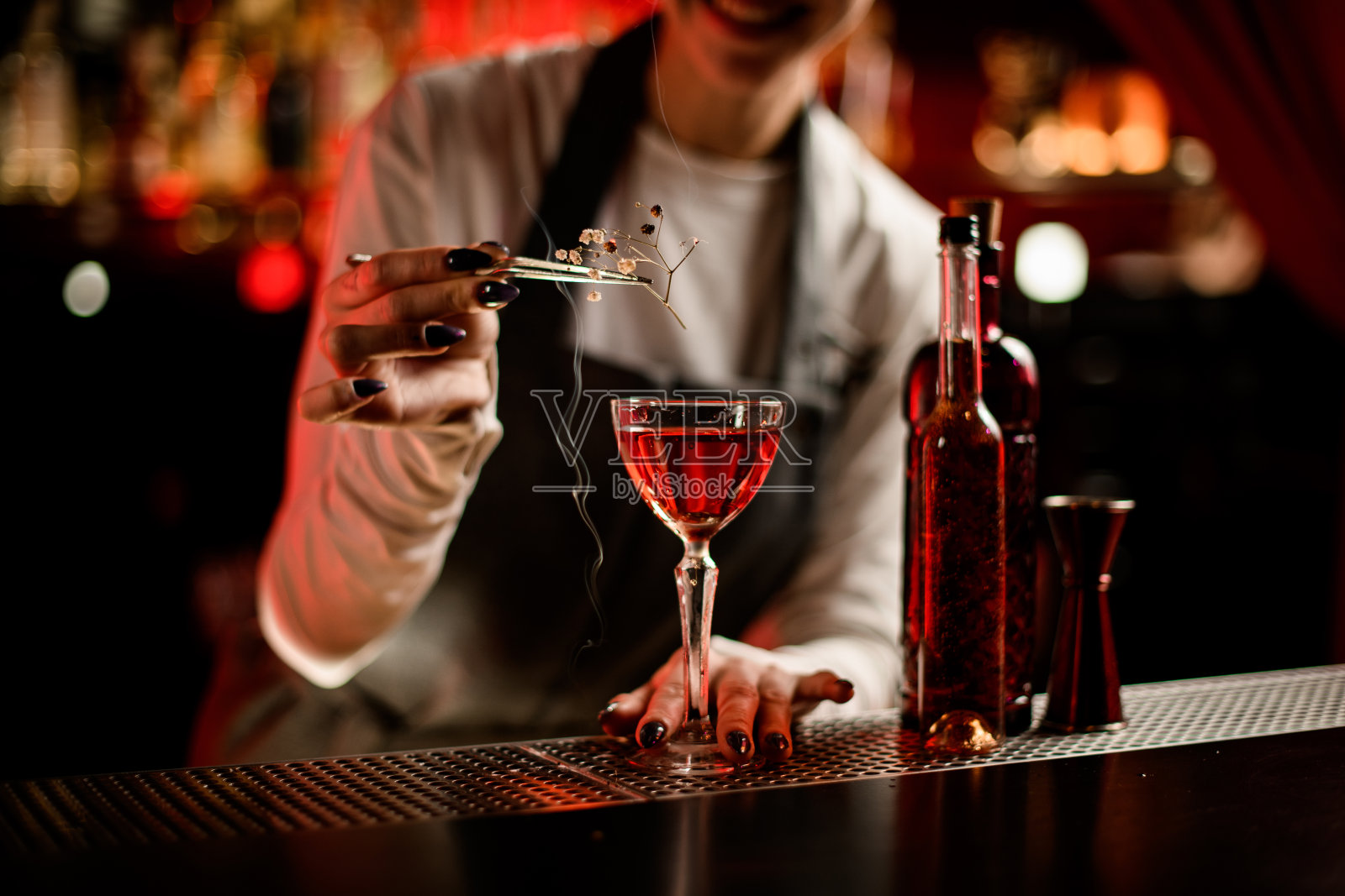 女酒保用闷烧的花枝装饰的酒杯照片摄影图片