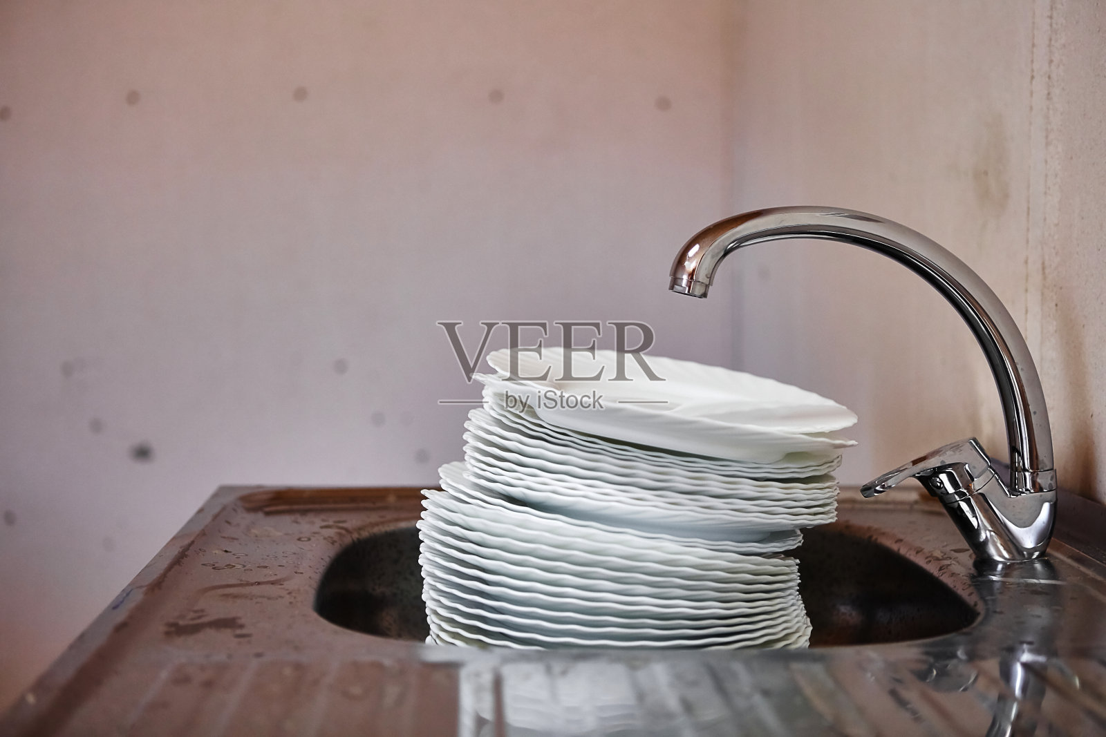 在肮脏的厨房里，水龙头下面的金属水槽里有一大堆脏瓷盘照片摄影图片