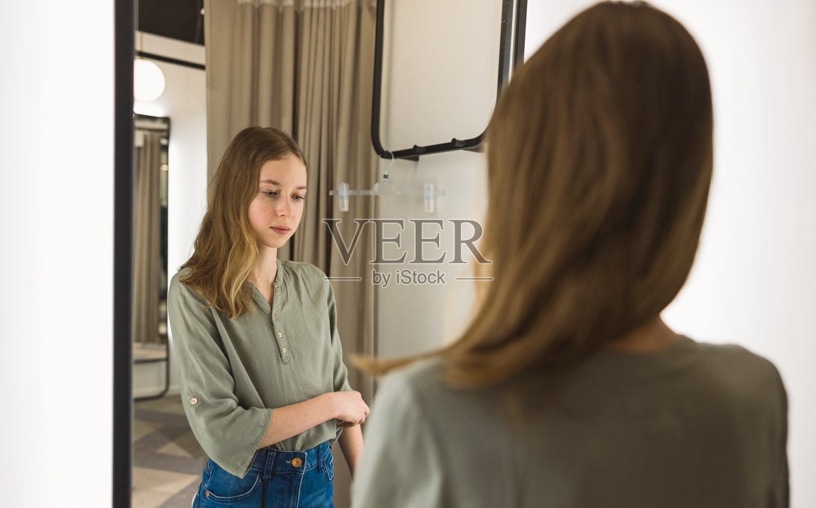 少女站在服装店的试衣间里。照片摄影图片