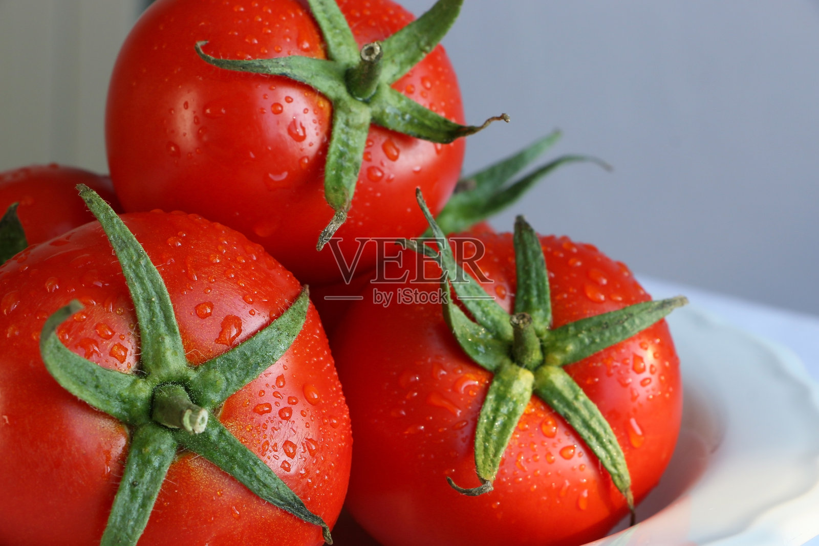 白瓷盘上鲜湿的红番茄，白色背景，自然光照片摄影图片